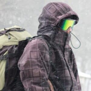 Portrait of a tourist  with a backpack in bad weather in the mountains. Heavy snowstorm. Face closed with a windproof mask. Extreme clothing. Close-up